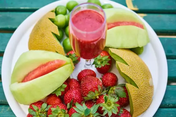 Strawberry fruit and juice inside the wine glass and some other fruits inside the white plate